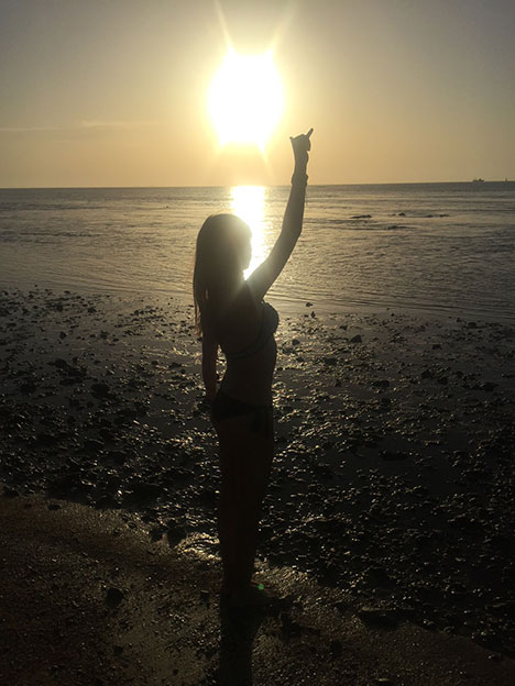 Imagen de mujer frente al mar bajo la puesta de sol